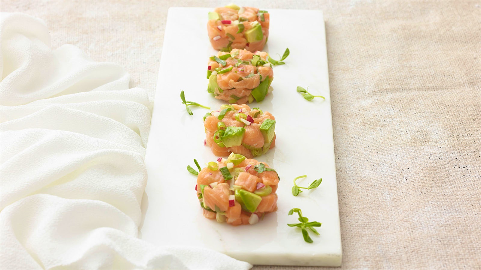  A serving plate with four discs of salmon and avocado tartare garnished with spring green 
